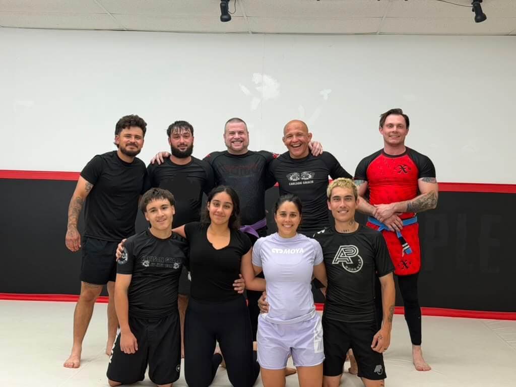 Adult students, men and women, with Professor Paraíba in front of the academy's black and red wall