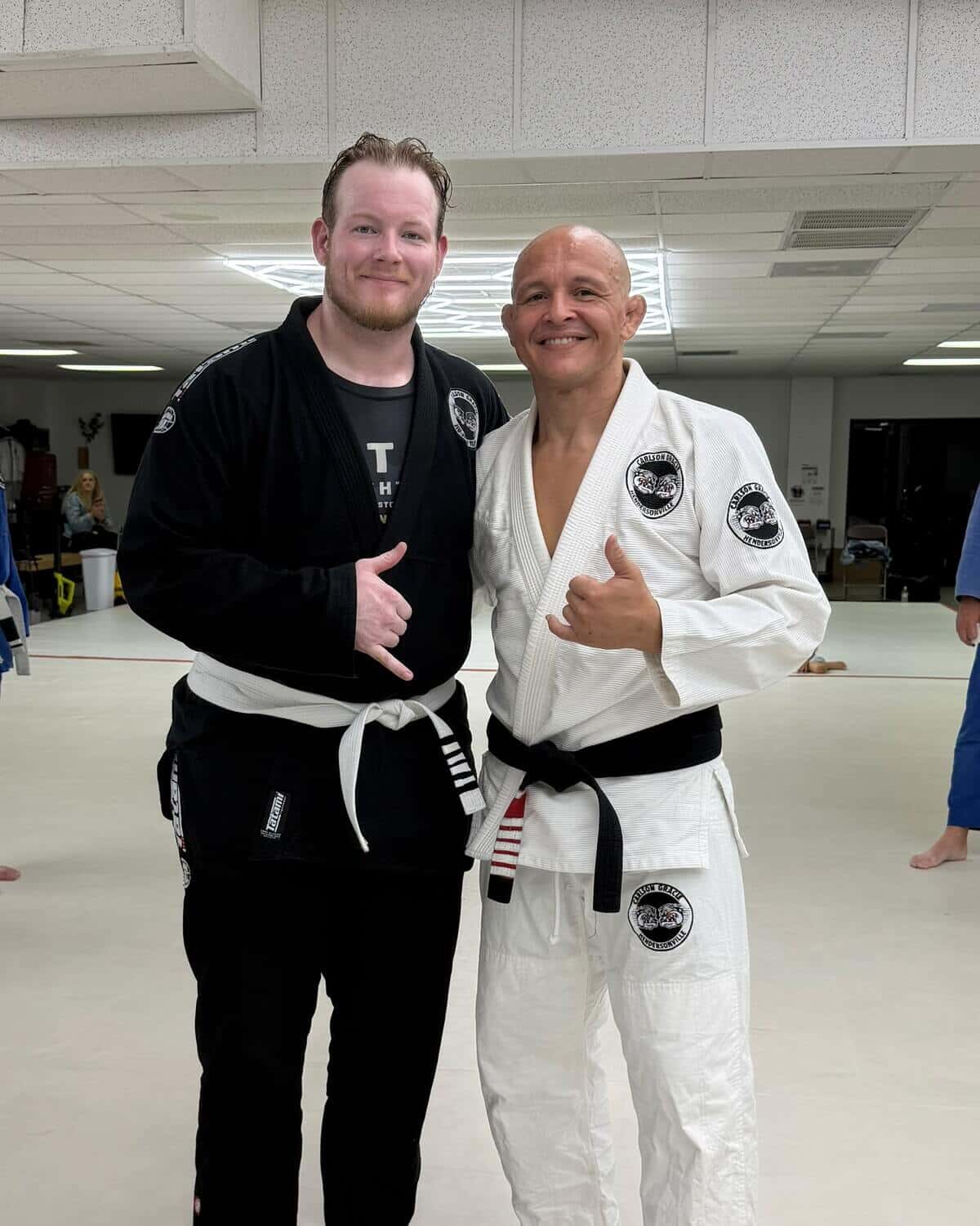 A new white belt student smiling next to Professor Paraíba on the mats at Carlson Gracie Hendersonville