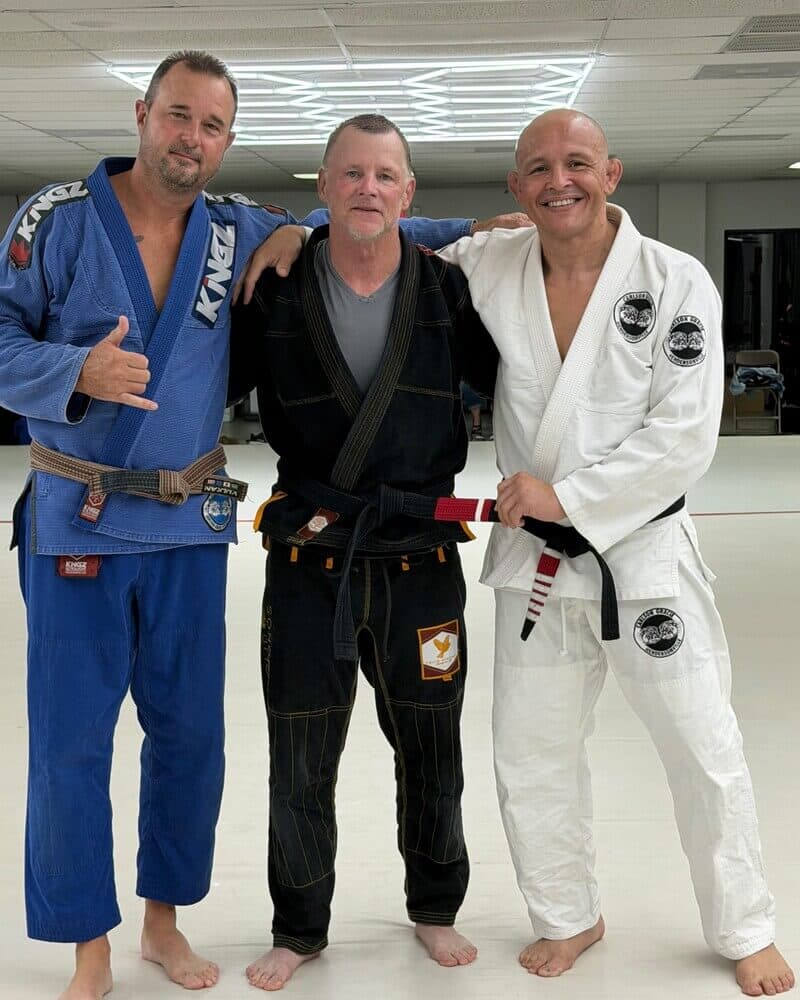 Two students standing with Professor Paraíba on the mats