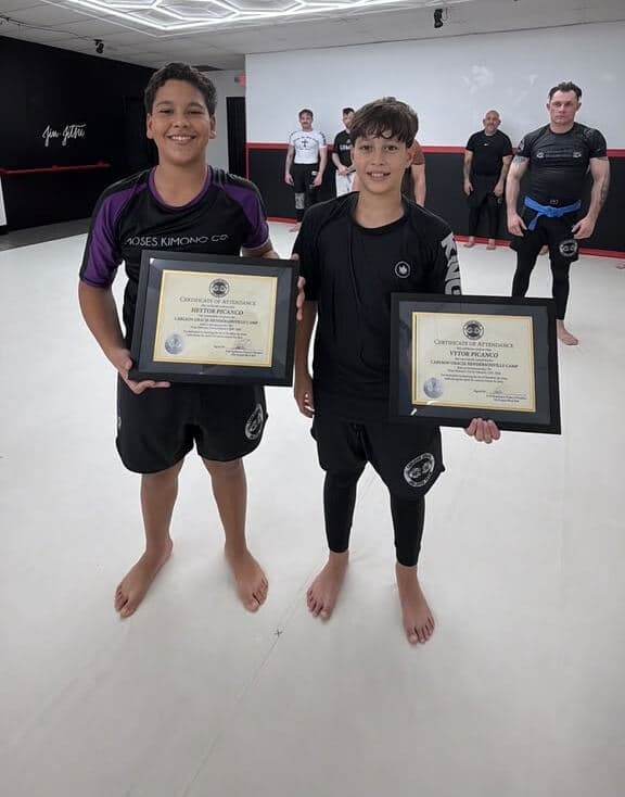 Two young students holding their certificates on the mats
